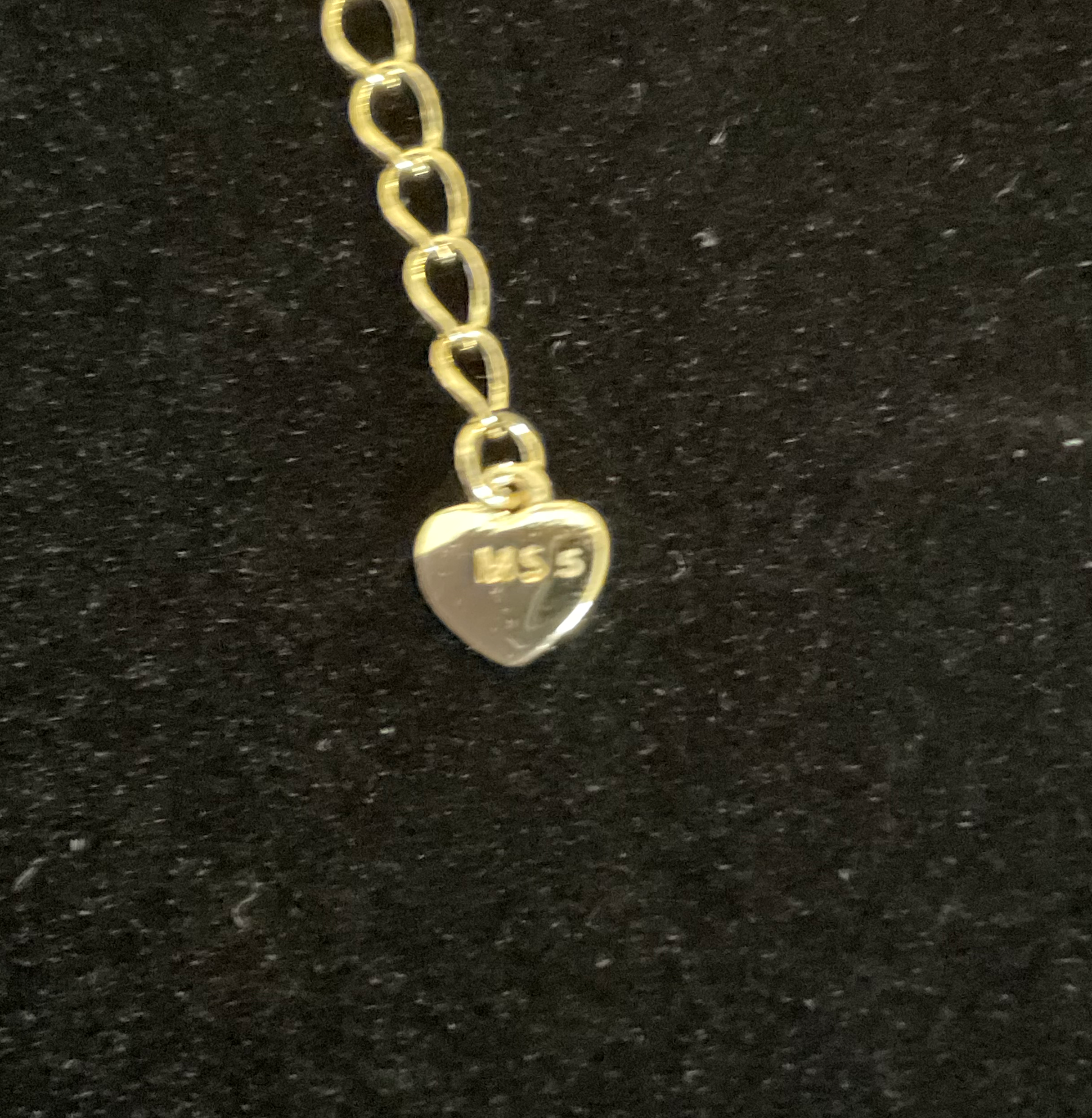Gold heart-shaped pendant with 'MSS' on a black background
