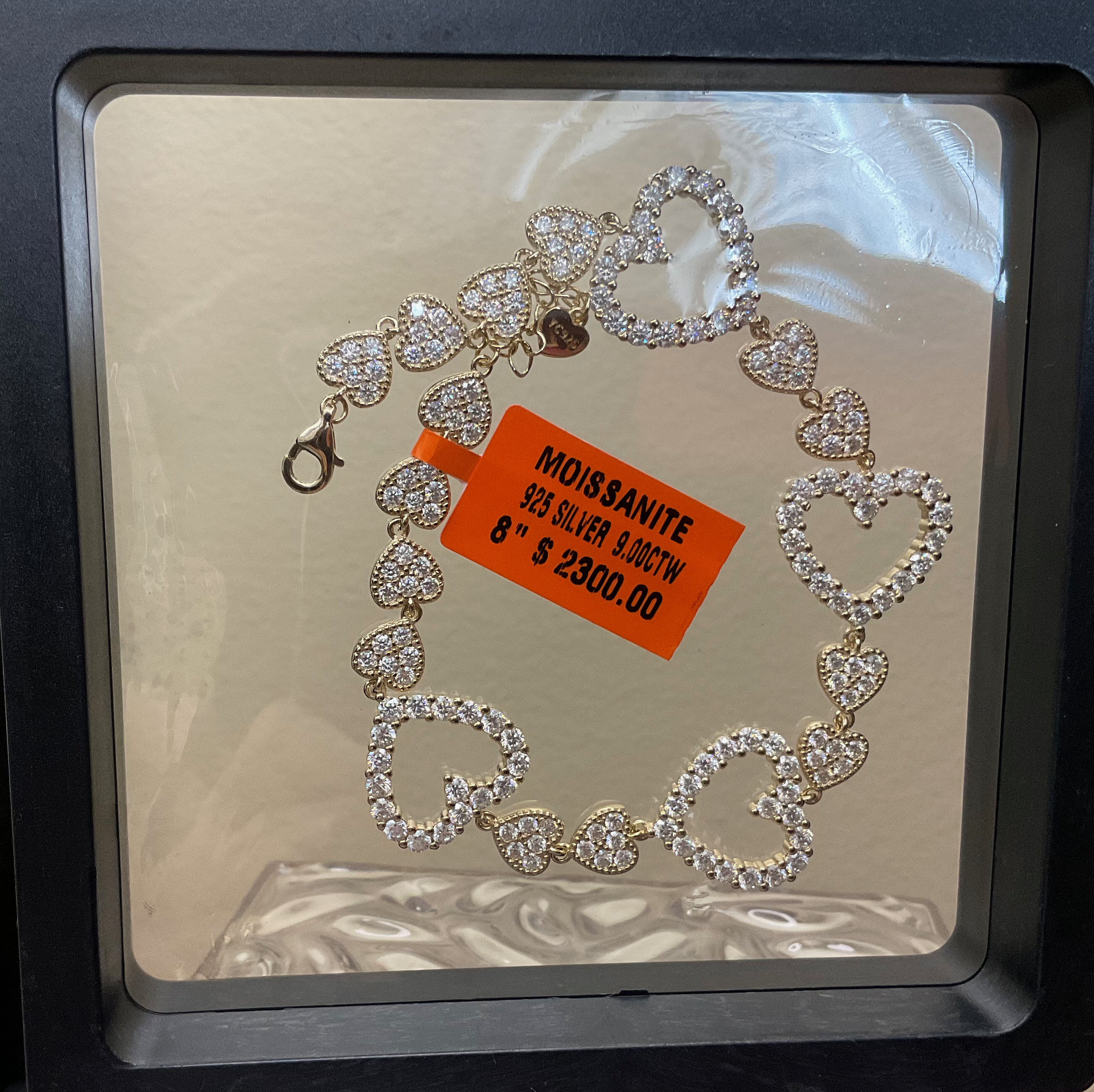 Heart-shaped bracelet with moissanite stones on a reflective surface