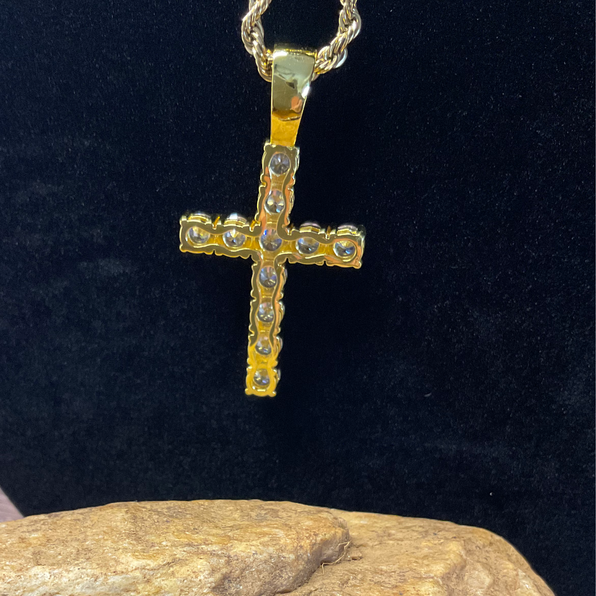 Gold cross pendant with clear stones on a black background