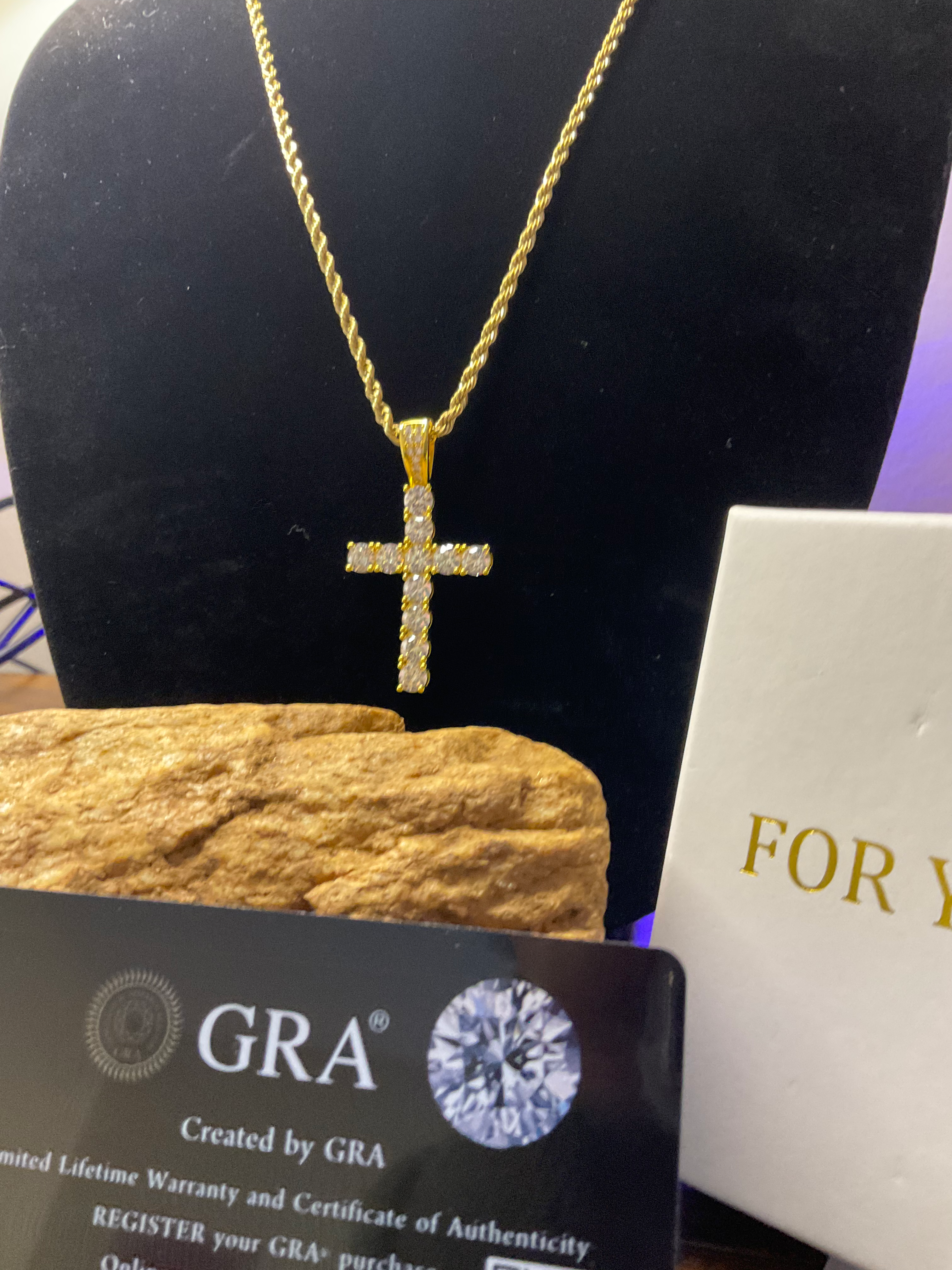 Gold cross pendant necklace on a black stand with GRA card and white box.