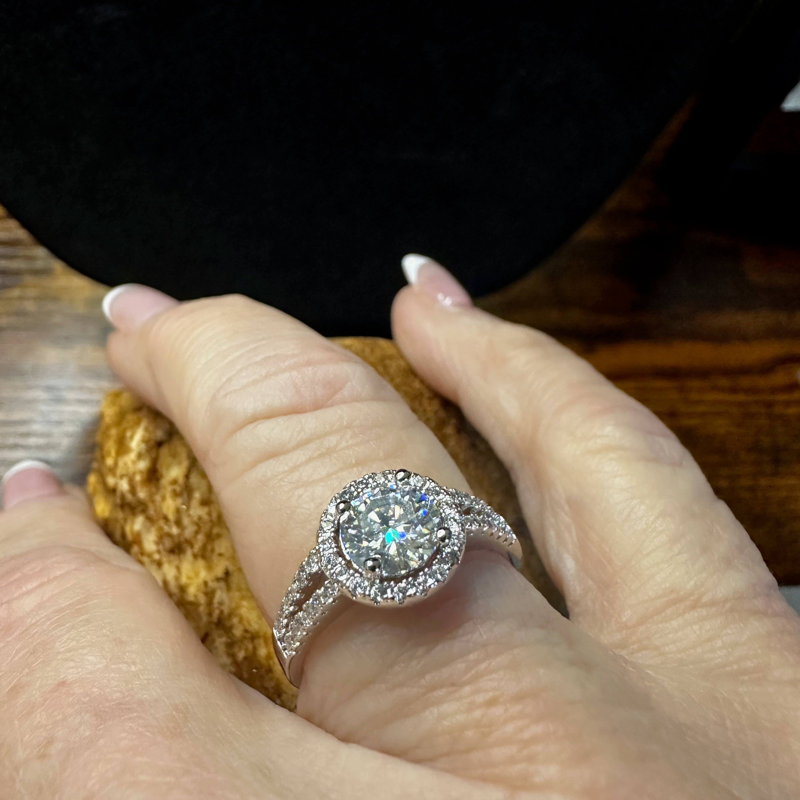 Close-up of a hand wearing a diamond ring on a wooden surface.