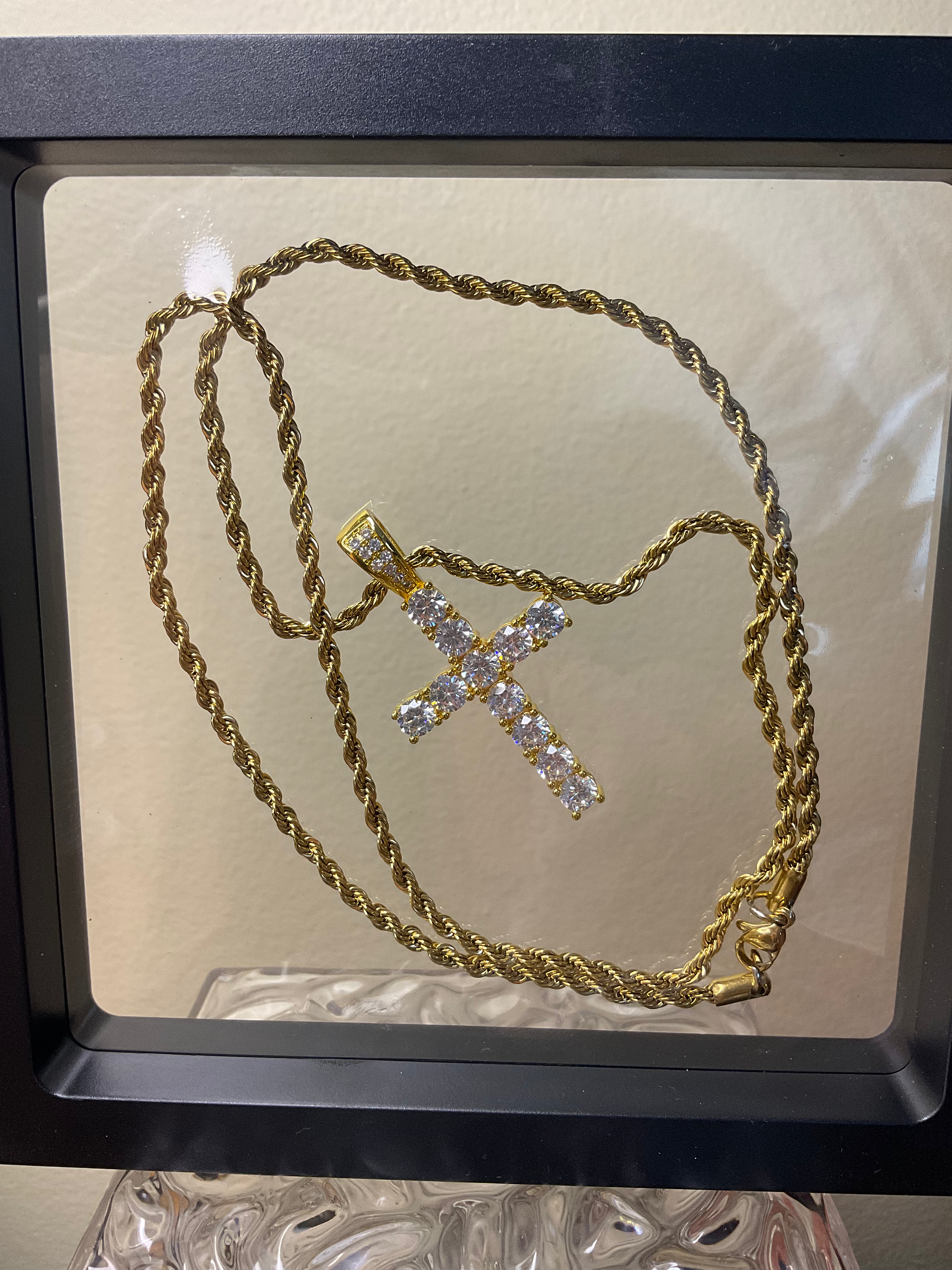 Gold necklace with a cross pendant on a reflective surface