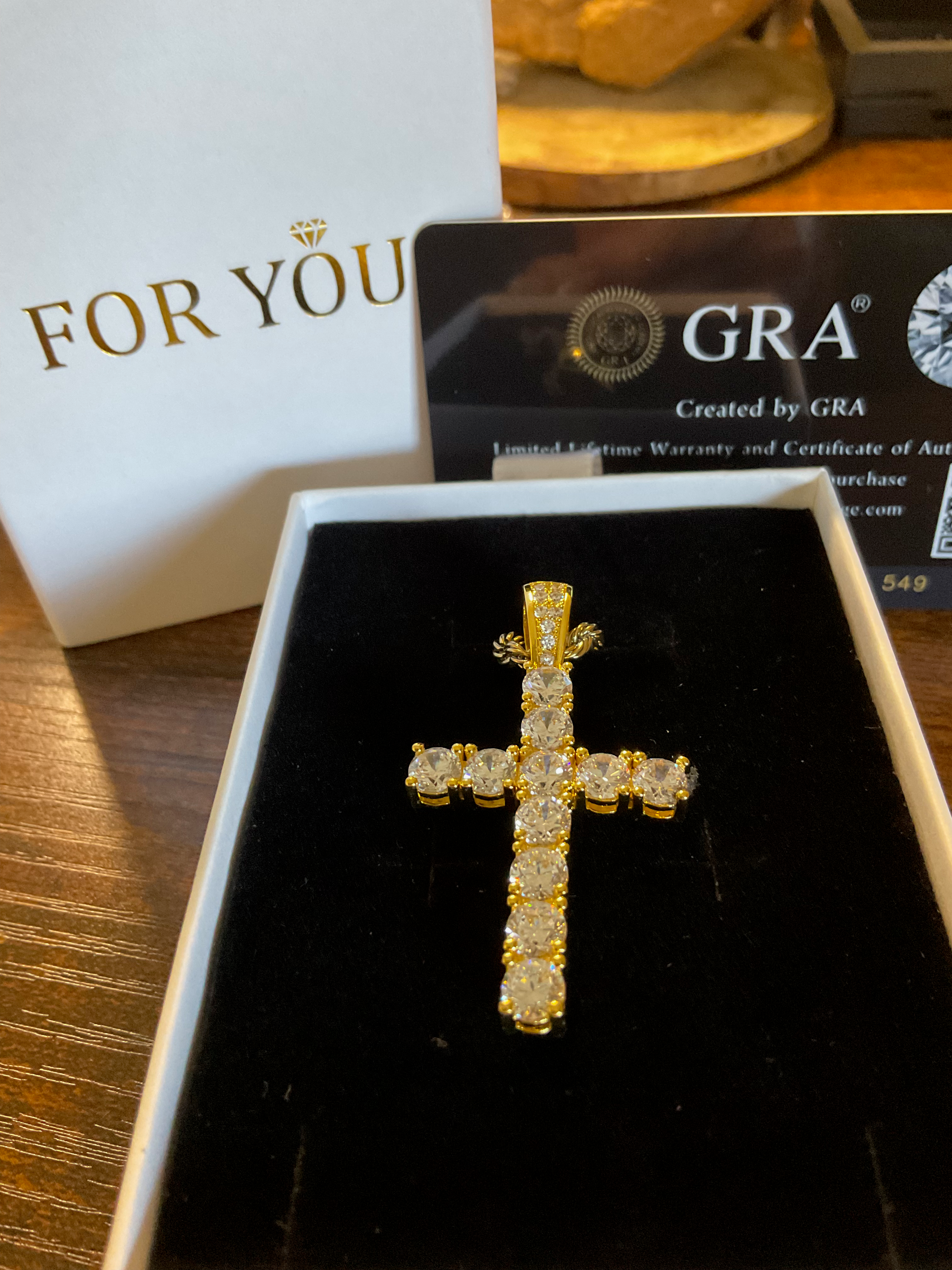 Gold cross pendant in a box with GRA certification in the background