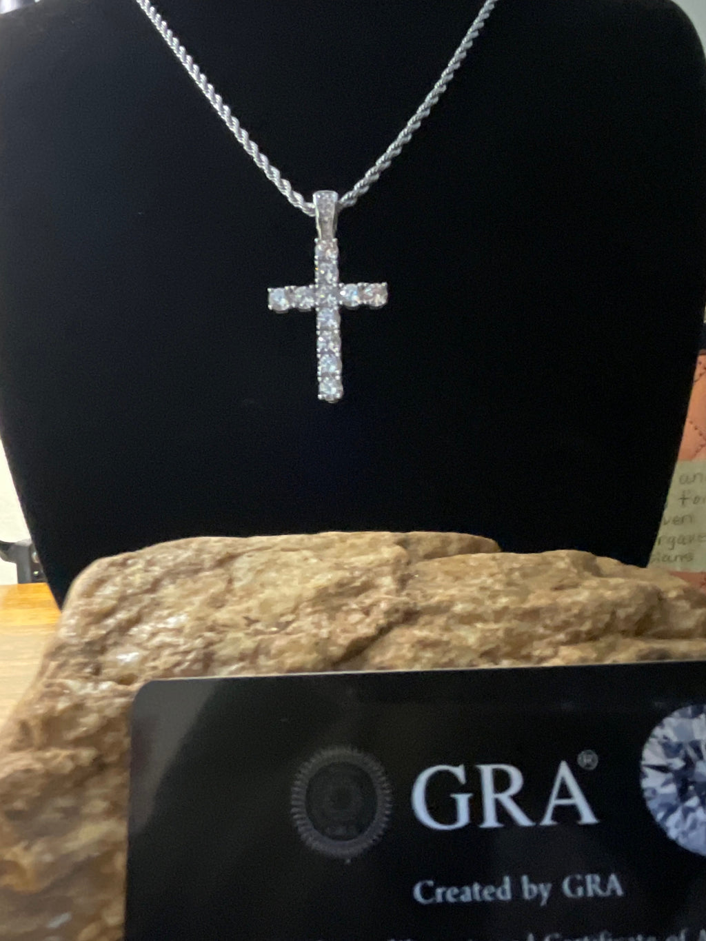 Silver cross pendant on a chain with a black card displaying 'GRA' branding.