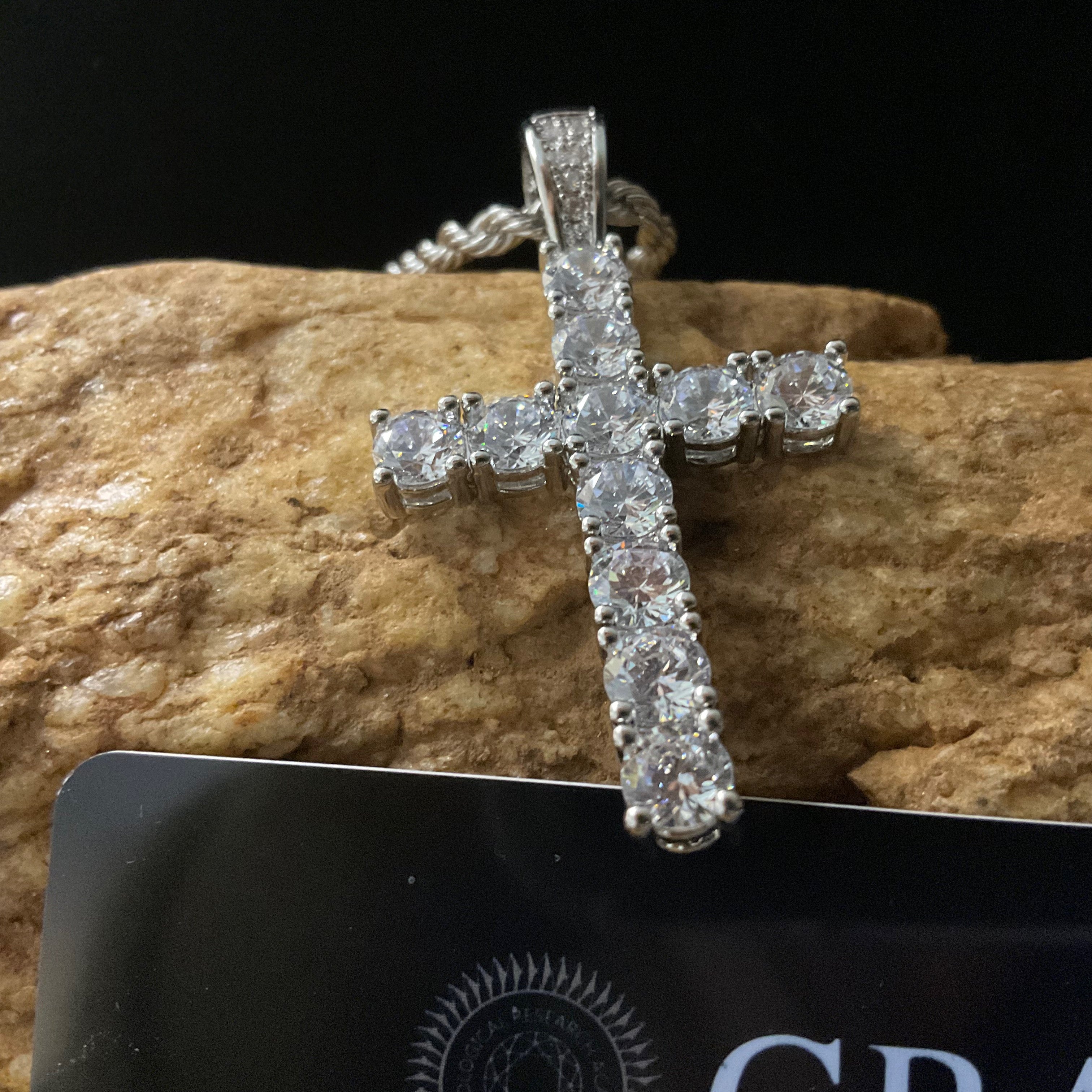 Silver cross pendant with clear stones on a dark background