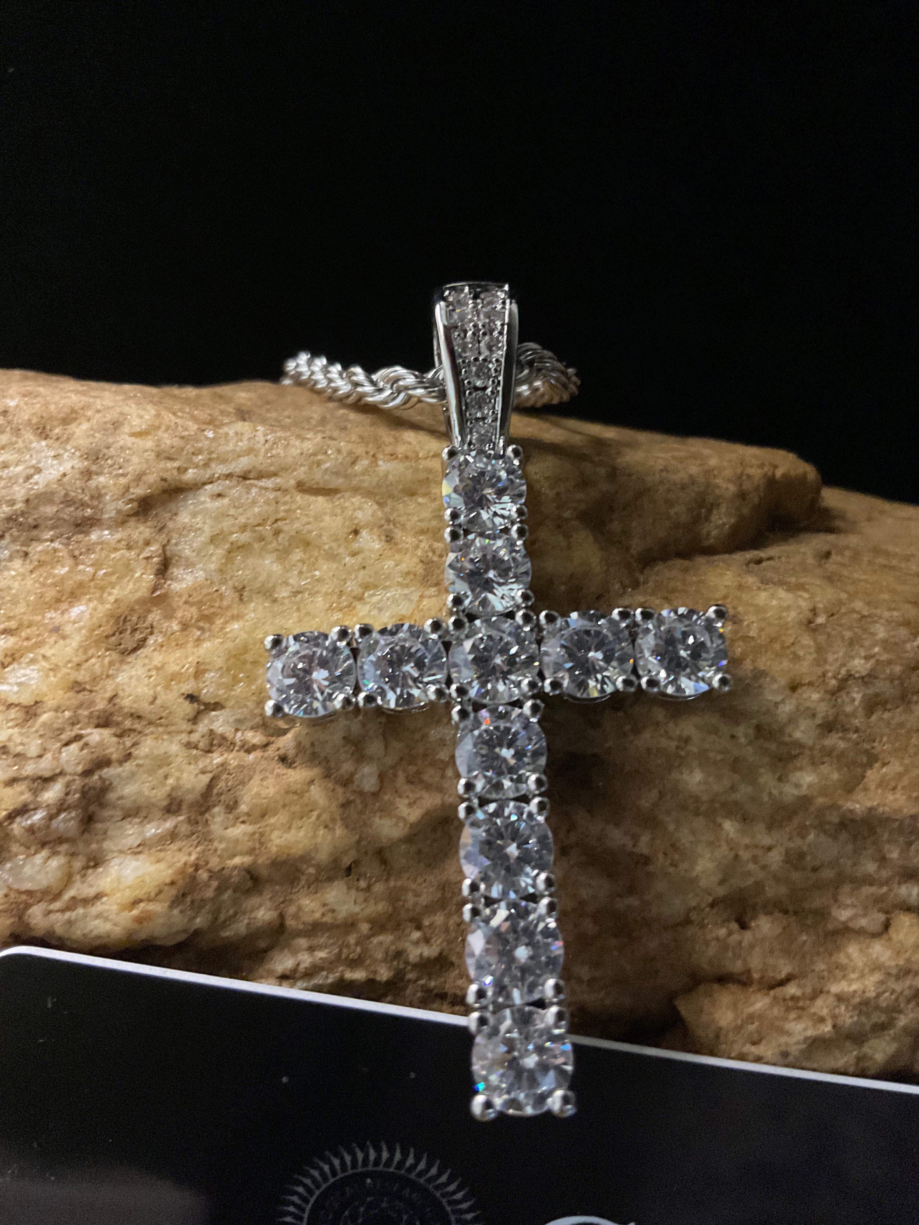 Silver cross pendant with clear stones on a rock background