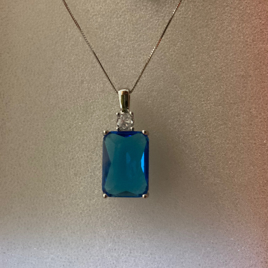 Blue gemstone pendant on a chain with a label on a plain background