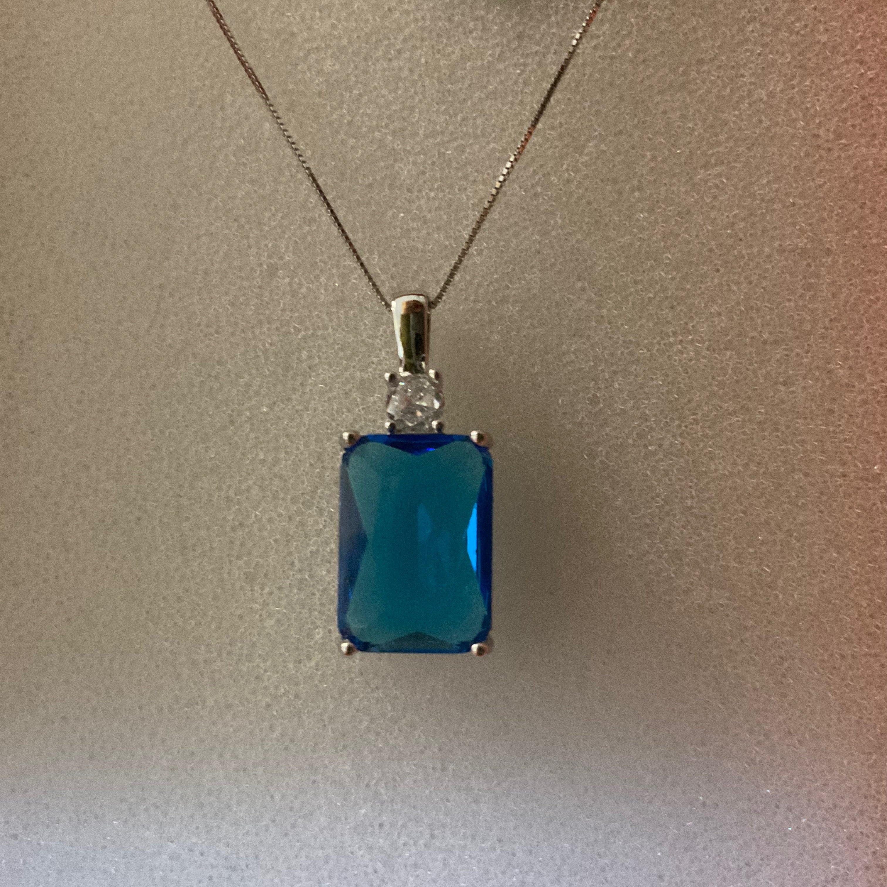 Blue gemstone pendant on a chain with a label on a plain background