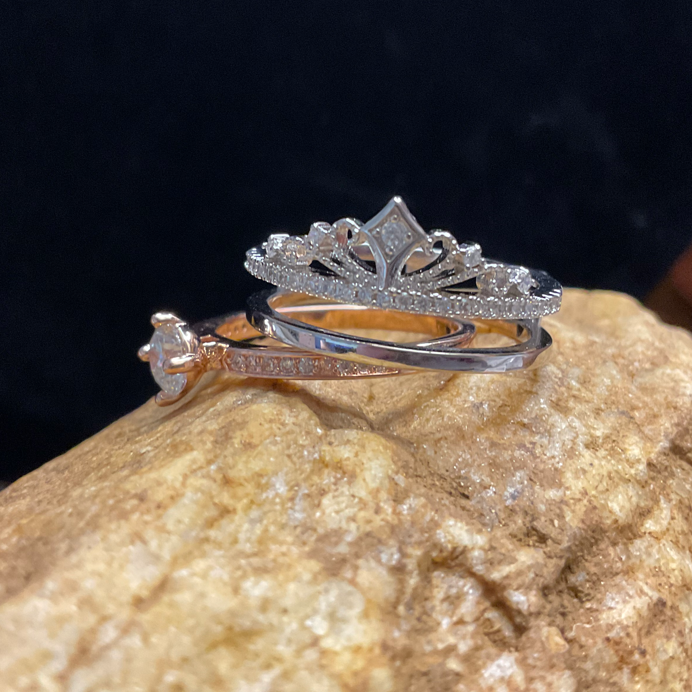 Two rings, one gold and one silver, on a rock with a dark background