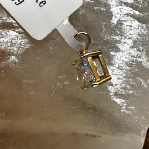 Gold pendant with gemstone on a textured surface with a price tag.