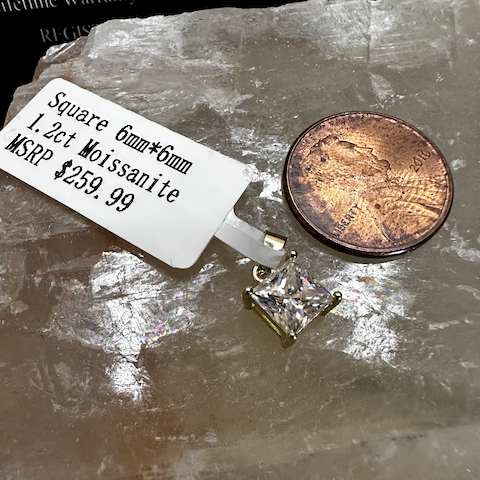 Square moissanite pendant on a stone surface with a penny for scale, next to a price tag.