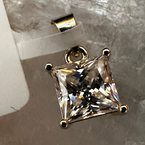 Gold pendant with a large clear gemstone on a gray surface