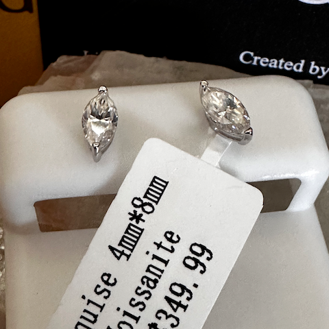Pair of marquise cut moissanite earrings on a white stand with a price tag.