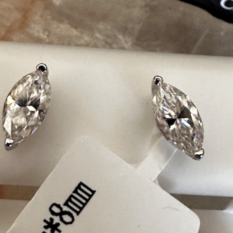 Pair of silver earrings with clear stones on a white surface, accompanied by a price tag.