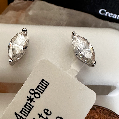 Pair of silver earrings with clear gemstones on a white stand with a label.