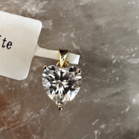 Heart-shaped gemstone pendant on a stone surface with a price tag.