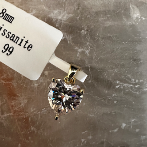 Heart-shaped moissanite pendant with price tag on a textured surface