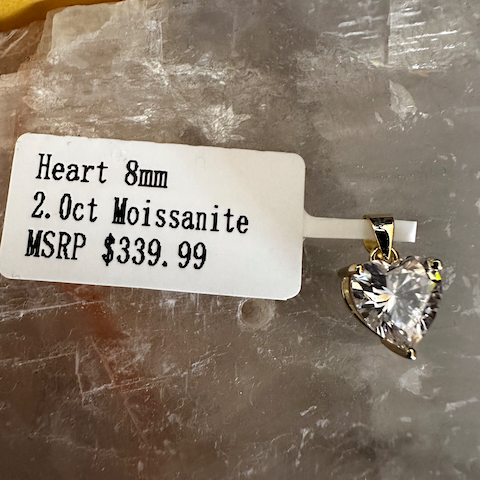 Heart-shaped moissanite pendant with price tag on a stone surface