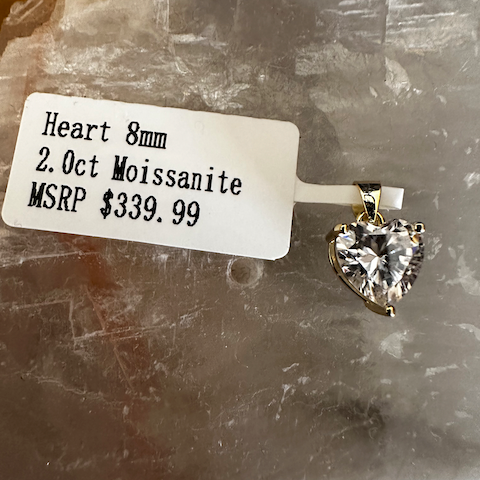 Heart-shaped moissanite pendant with a price tag on a textured surface