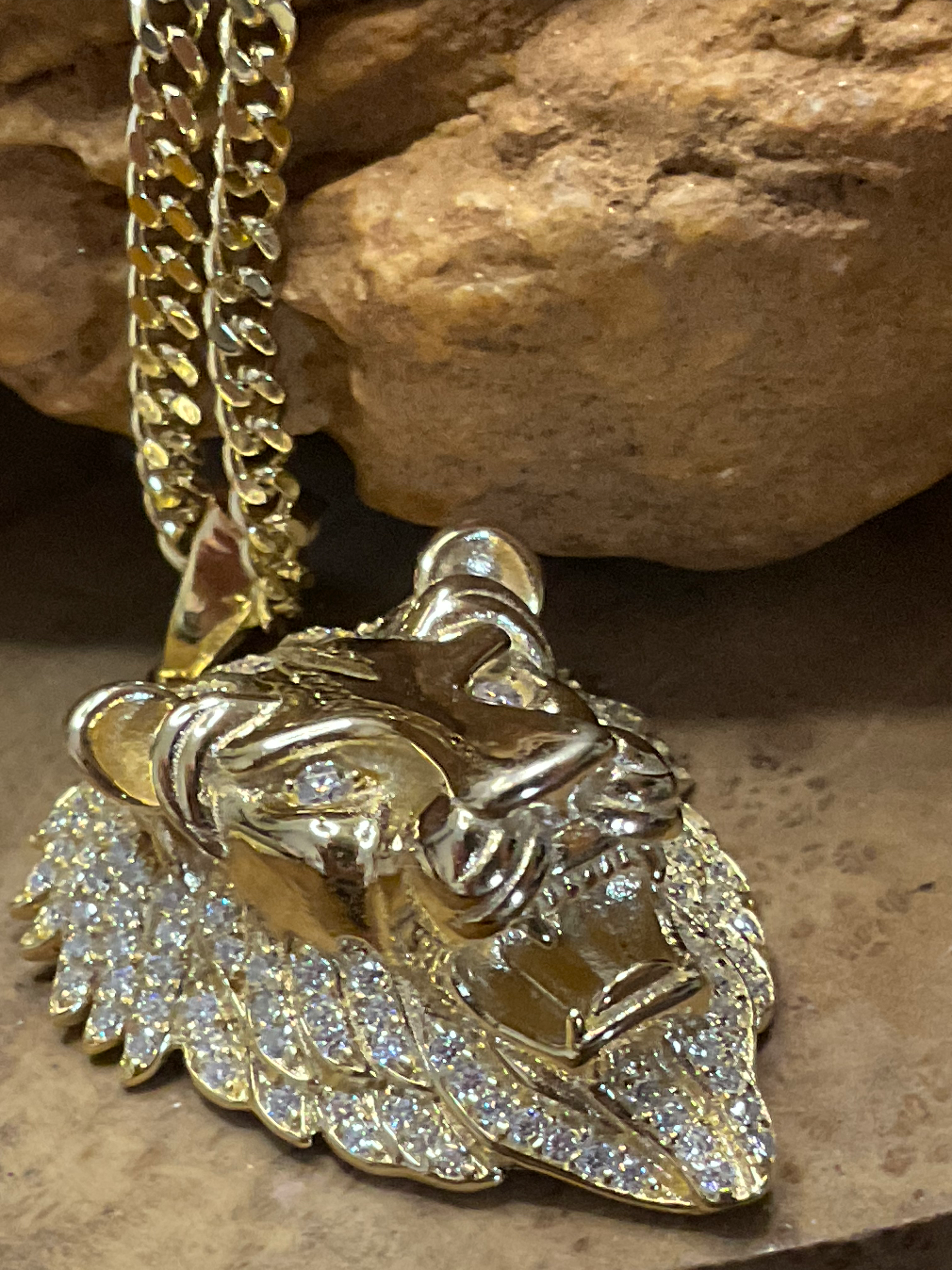 Gold lion pendant necklace with chain on a stone background