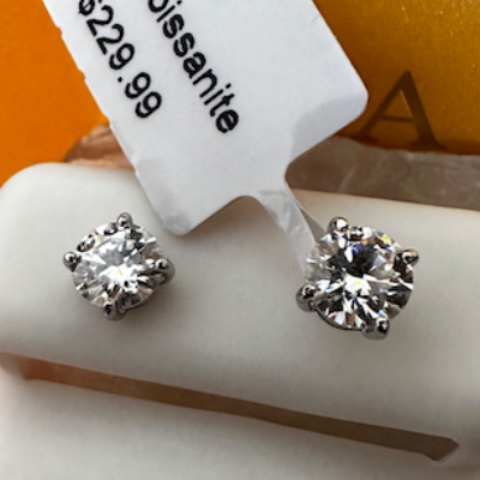 Pair of diamond earrings on a Moissanite branded stand with a price tag.