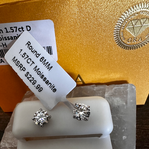 Round 6MM Moissanite earrings on a display card with gold background
