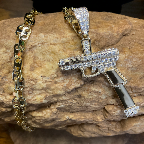 Gold bracelet and gun-shaped pendant on a stone surface