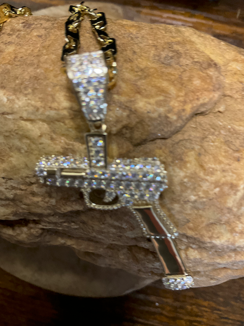 Gold and silver gun-shaped pendant on a chain, placed on a textured surface.