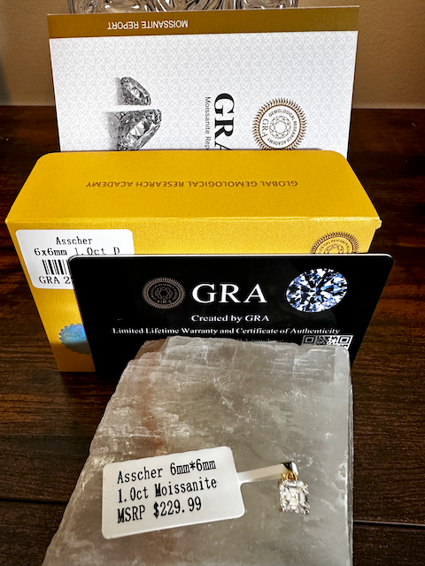 Asscher-cut moissanite diamond with GRA certification and packaging on a wooden surface