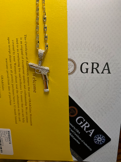 Gold necklace with a cross pendant on a yellow and white background with 'GRA' branding.