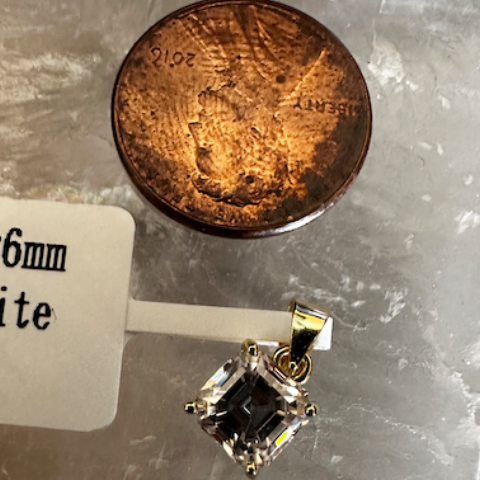 Silver pendant with a black stone next to a penny on a marble surface