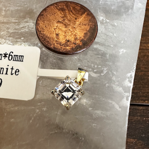Diamond pendant on a stand with a coin for scale, against a dark background with 'GRA' branding.