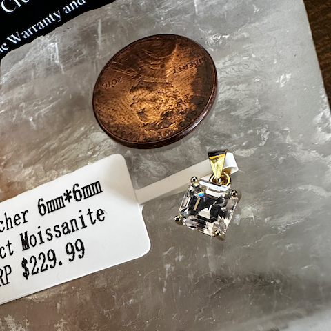 Diamond pendant next to a penny on a marble surface with a price tag.