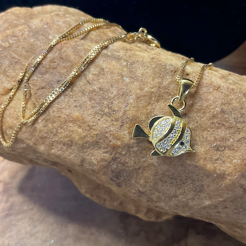 Gold necklace with a fish-shaped pendant on a stone surface