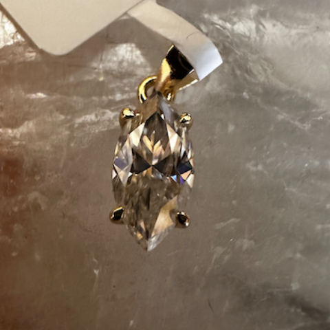 Gold pendant with clear gemstone on a textured surface, with a price tag attached.