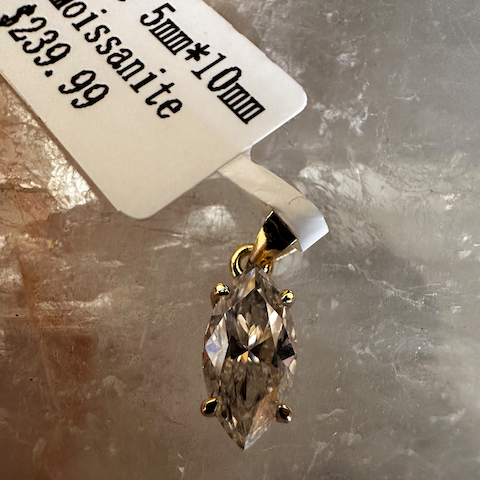 Diamond pendant with gold setting on a gray surface, accompanied by a price tag.
