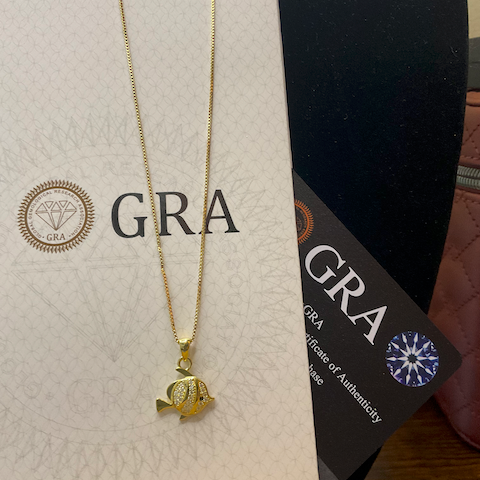 Gold necklace with a fish pendant on a GRA branded box