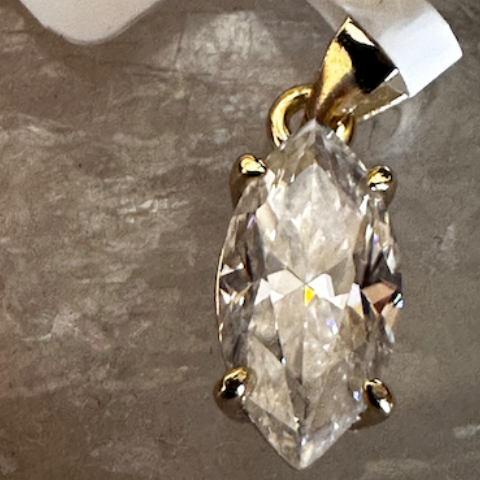 Gold pendant with a large clear gemstone on a gray surface