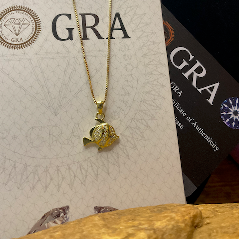Gold necklace with a fish pendant on a GRA branded card.