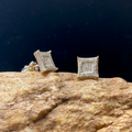Gold square stud earrings on a textured stone surface with a dark background