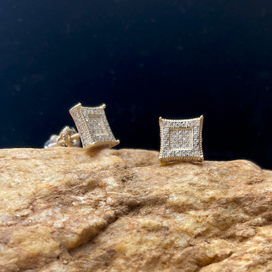Gold square stud earrings on a textured stone surface with a dark background