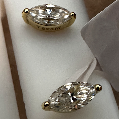 Gold earrings with marquise-shaped diamonds on a white stand.
