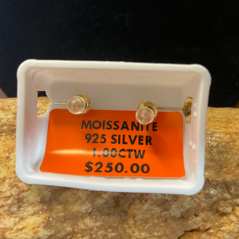 Small earrings on a display card with text about moissanite and silver content, against a dark background.