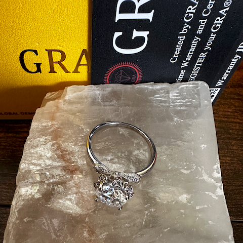 Silver ring with a diamond on a stone surface with 'GRA' branding in the background.