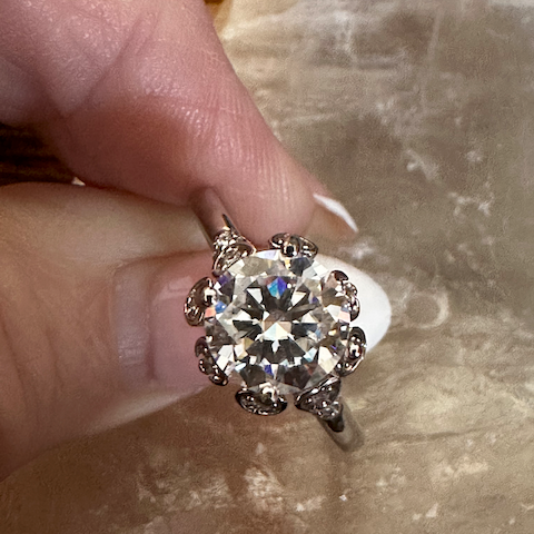 Diamond ring held between fingers on a textured surface