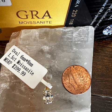 Diamond earring on a clear stone with a penny for scale, against a background with 'GRA' branding.