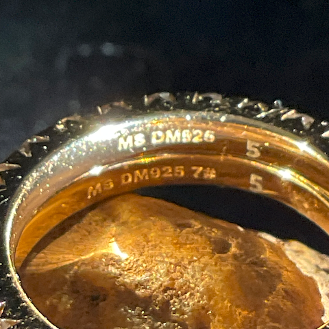 Gold ring with a large stone and diamond-studded band on a dark background