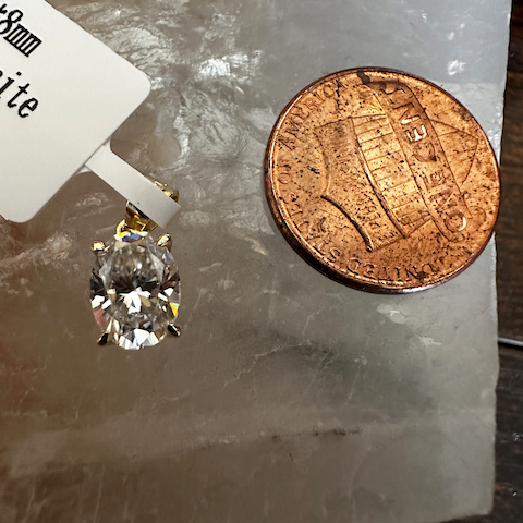 Diamond earring next to a penny on a marble surface