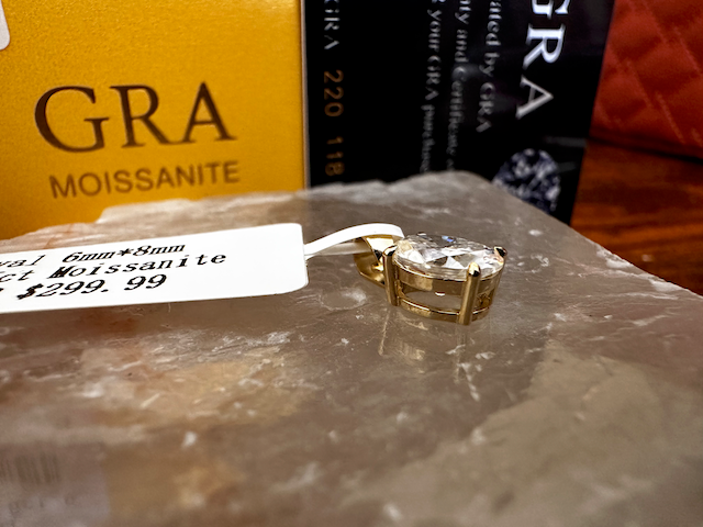 Gold ring with Moissanite on a clear surface, with 'GRA' branding in the background.