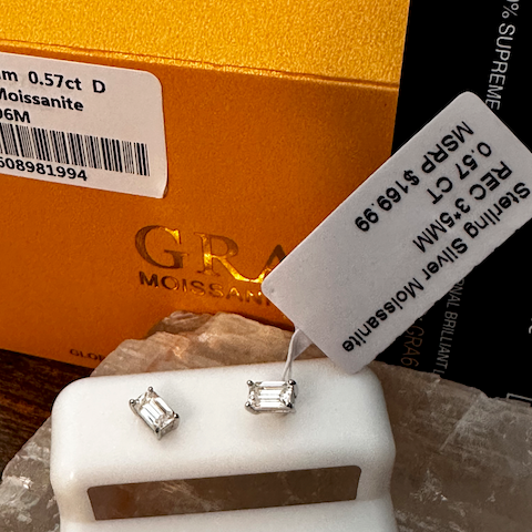 Diamond earrings on a white stand with a gold box and label in the background